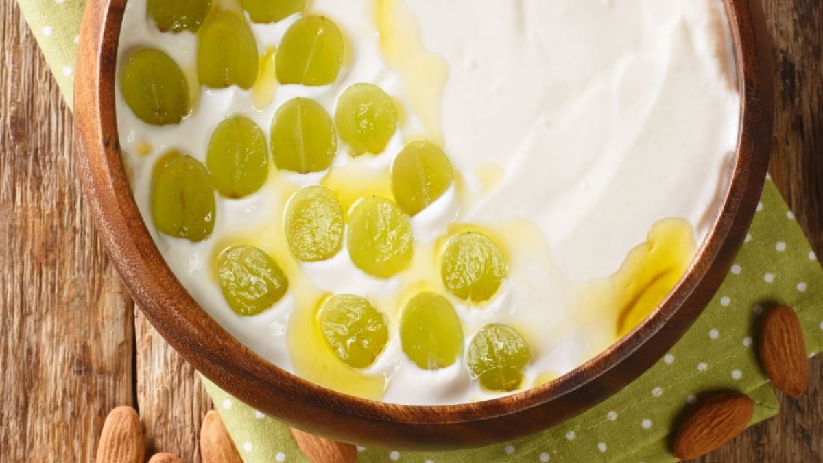 Traditionele Ajoblanco, romige witte koude soep uit Andalusië, geserveerd met groene druiven en olijfolie in een houten kom met amandelen ernaast