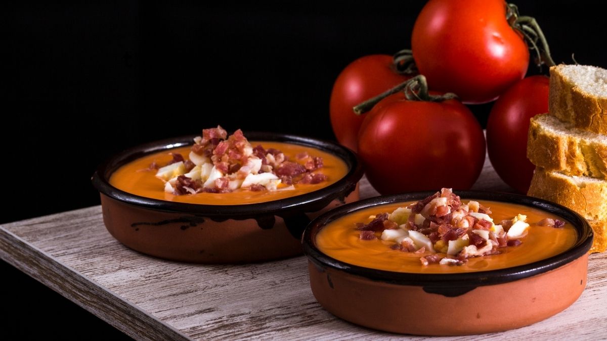 Traditionele salmorejo in aardewerken schaaltjes, gegarneerd met ei en serranoham, geserveerd met brood en tomaten – een Andalusisch streekgerecht
